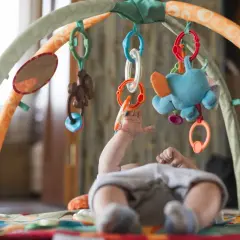 Niemowlę bawi się zabawkami wiszącymi na macie edukacyjnej.
