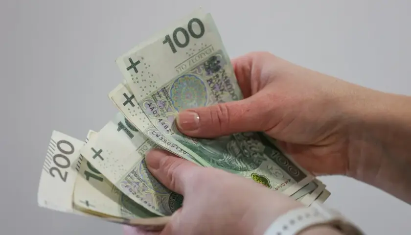 Dłonie trzymające polskie banknoty 100 i 200 zł.